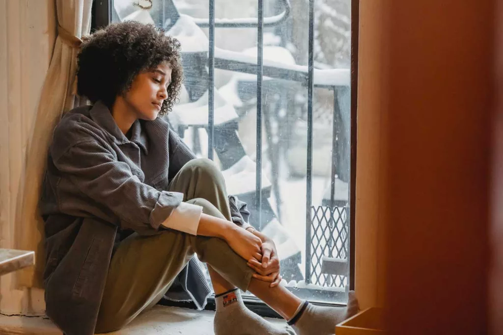 A woman with symptoms of Seasonal Affective Disorder (SAD), sitting by a window in Winter.