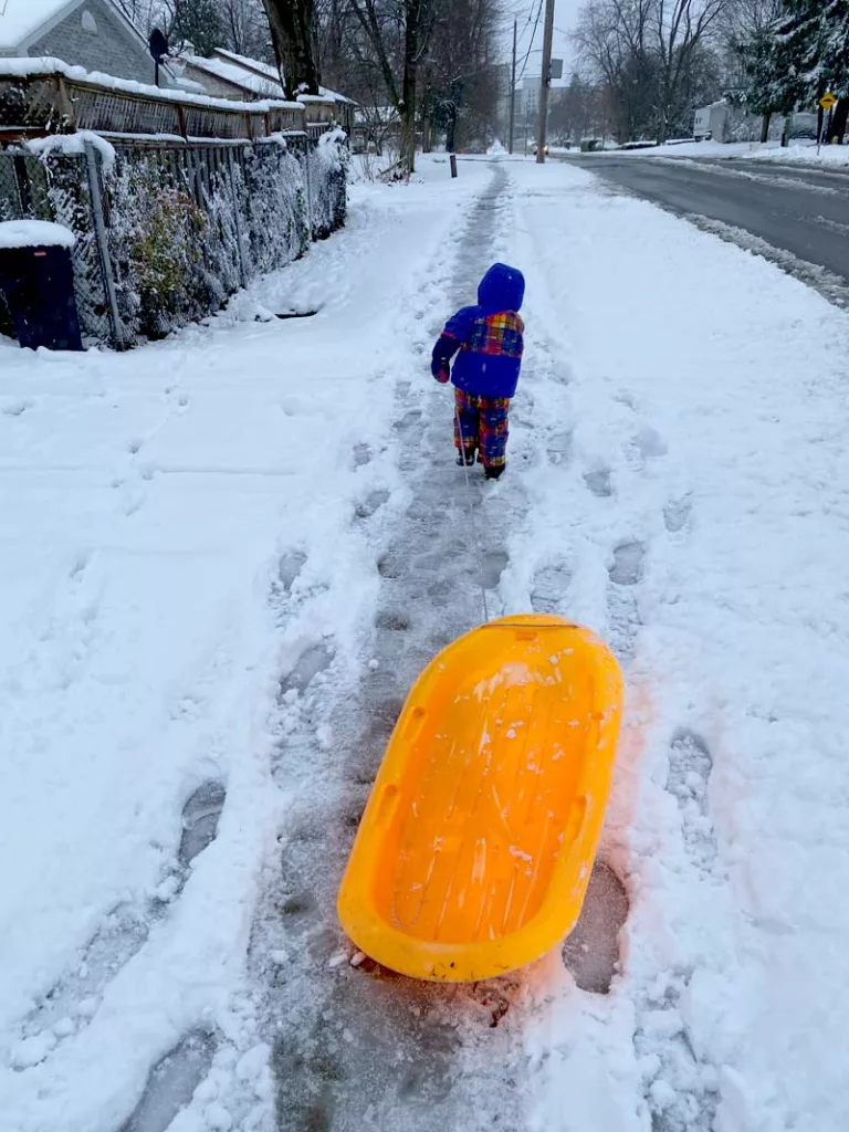 A child pulling a sled in a city in the winter.